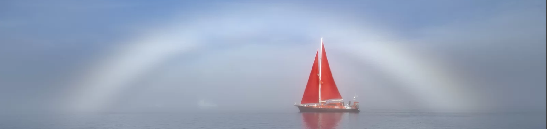 Red sailboat in front of a fogbow